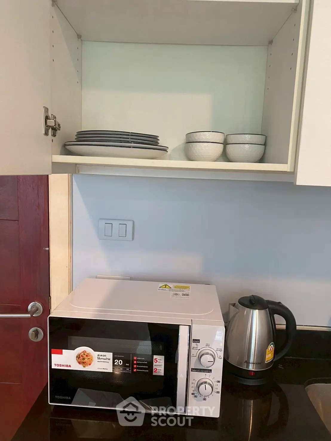 Modern kitchen corner with microwave, kettle, and neatly arranged dishes in cabinet.