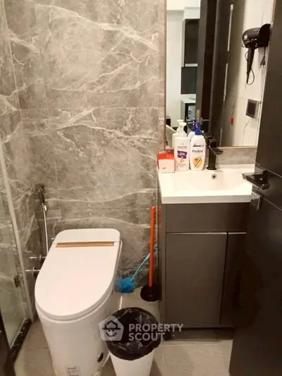 Modern bathroom with sleek fixtures and marble walls, featuring a compact vanity and toilet.