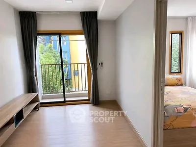 Bright living room with balcony access and view of greenery, adjacent to cozy bedroom.