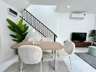 Modern dining area with stylish furniture and indoor plants, featuring a sleek staircase and wall-mounted air conditioning.