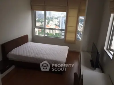 Cozy bedroom with city view, featuring a comfortable bed and large windows for natural light.