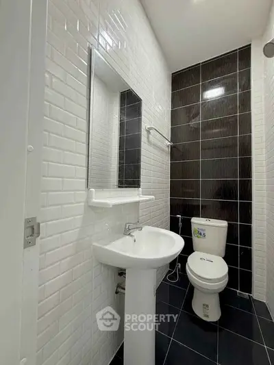Modern bathroom with sleek black and white tiles, featuring a pedestal sink and toilet.