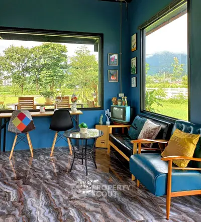 Charming living room with large windows and scenic garden view, featuring stylish furniture and vibrant decor.