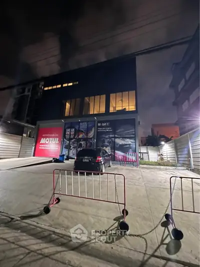 Modern commercial building exterior with large glass windows and parking area at night.