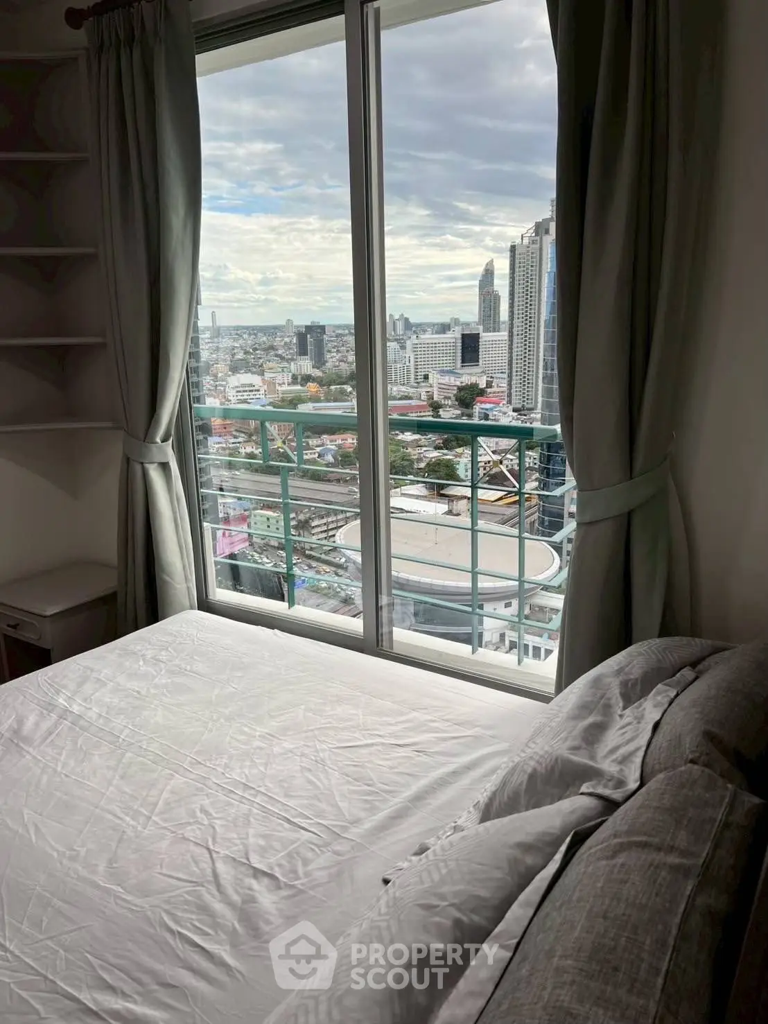 High-rise bedroom with stunning city view through large window, modern and cozy ambiance.