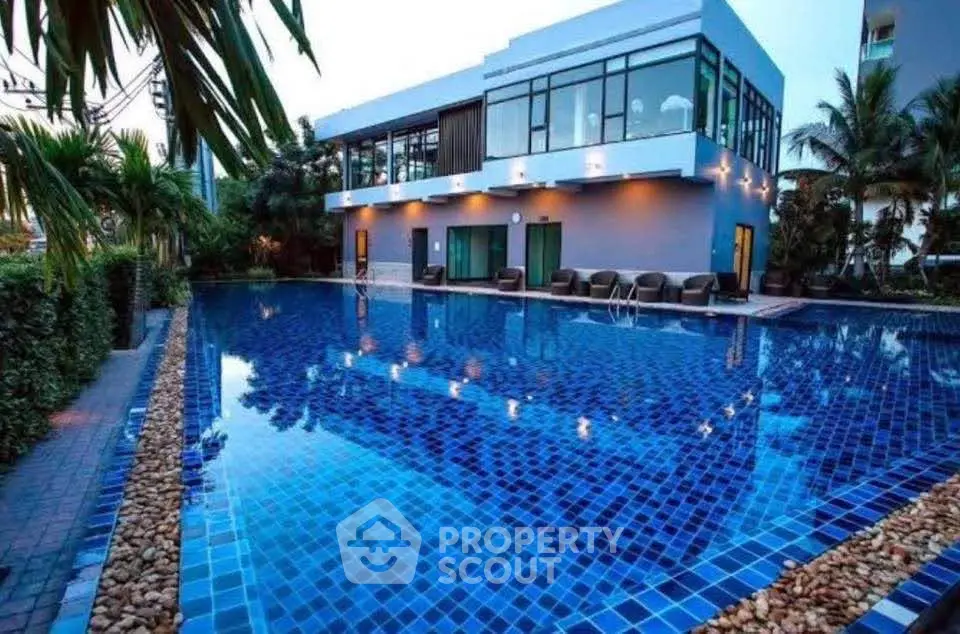 Luxurious modern building with a stunning blue-tiled swimming pool surrounded by lush greenery.