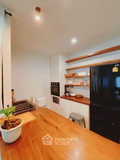Modern kitchen with sleek black fridge and wooden countertops, featuring open shelving and built-in oven.