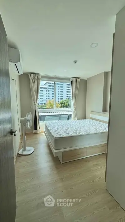 Bright and airy bedroom with large window and modern furnishings in a high-rise apartment.