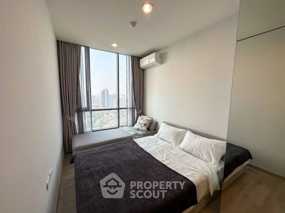 Modern bedroom with large window offering stunning city views and cozy furnishings.