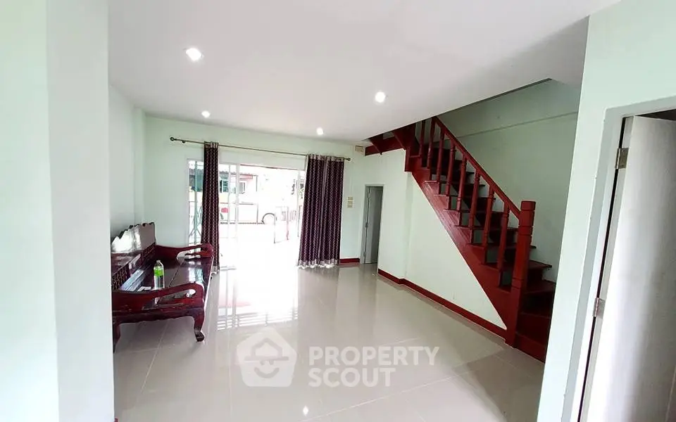 Spacious living room with elegant staircase and large windows for natural light.