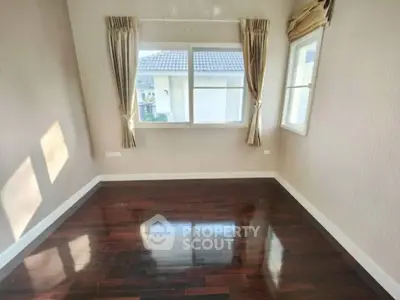 Spacious room with polished wooden floors and large windows offering natural light.