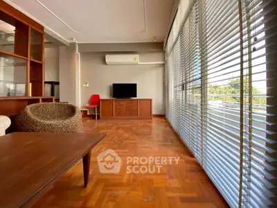 Spacious living room with wooden flooring and large windows with blinds, featuring modern furniture.