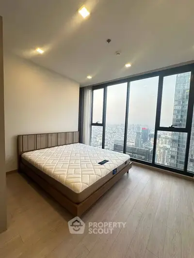 Spacious bedroom with stunning city view and large windows in modern high-rise apartment.