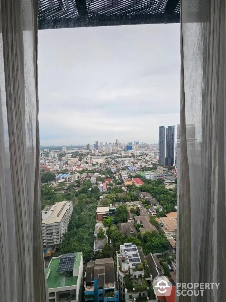 Stunning cityscape view from high-rise apartment window with sheer curtains framing the skyline.