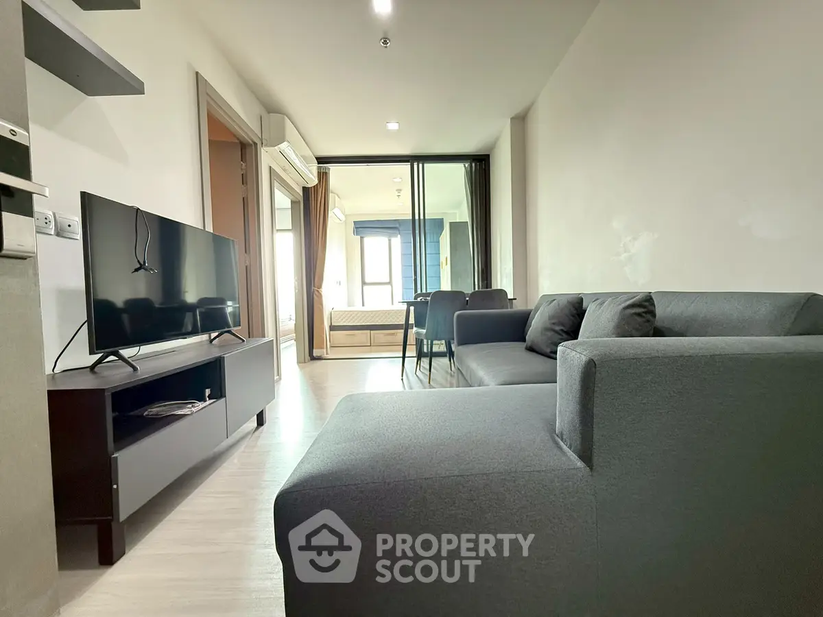 Modern living room with sleek gray sofa and TV, open layout leading to bedroom.