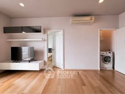 Modern living room with wooden flooring, TV unit, and washing machine in a sleek apartment.