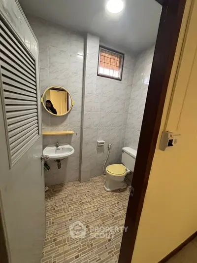 Cozy bathroom with tiled walls and floor, featuring a round mirror and compact layout.