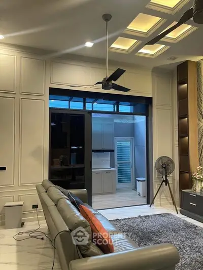 Luxurious living room with modern ceiling fan and elegant decor, leading to a stylish kitchen area.