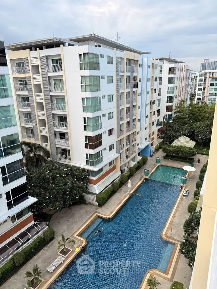 Stunning aerial view of modern apartment complex with large swimming pool and lush greenery.