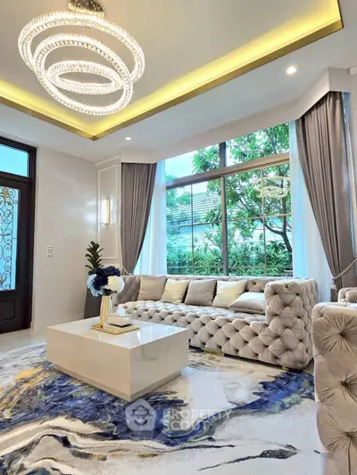 Luxurious living room with elegant chandelier and plush sofa, featuring large windows and stylish decor.