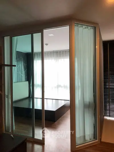 Modern bedroom with glass walls and wooden flooring, featuring a minimalist design.