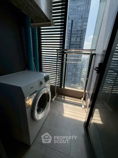 Modern high-rise apartment balcony with washing machine and city view.