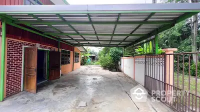 Spacious covered parking area with open gate and lush greenery, perfect for multiple vehicles.