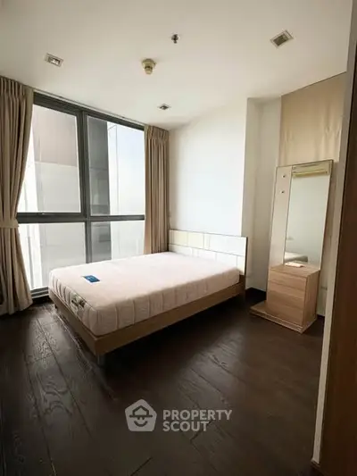 Modern bedroom with large window and wooden flooring in a stylish apartment.