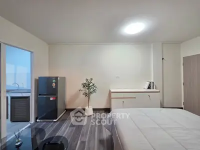 Modern bedroom with sleek flooring and compact kitchenette, featuring a mini fridge and stylish decor.