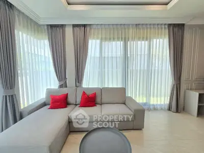 Bright living room with large windows and modern gray sofa accented by red pillows.