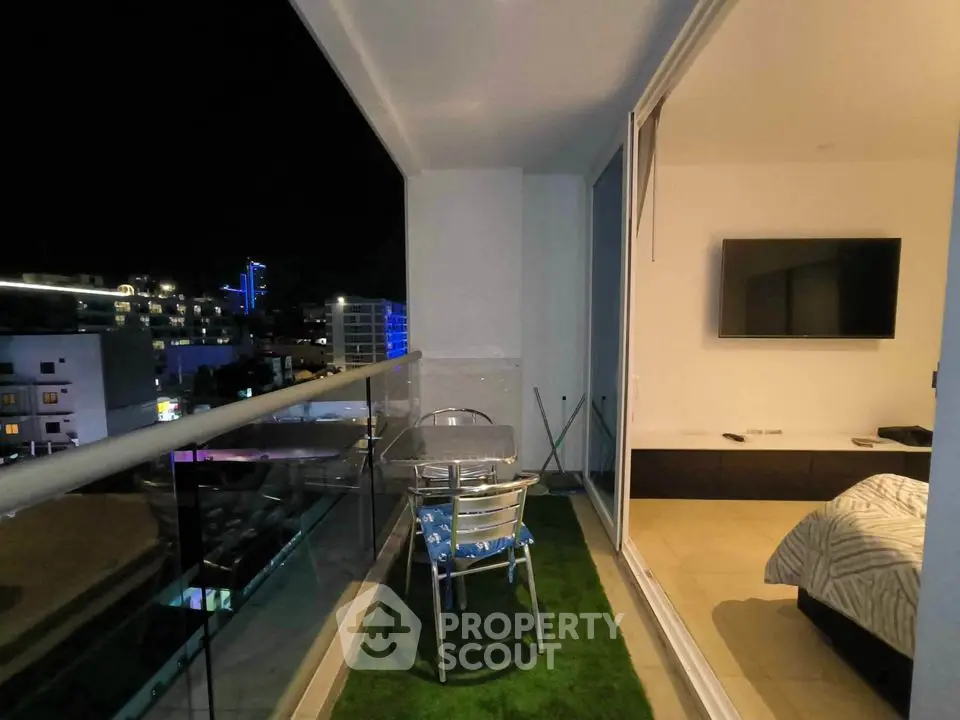 Modern apartment balcony with night city view and cozy seating area.
