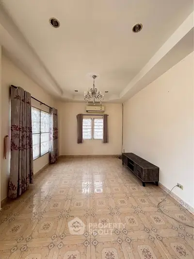 Spacious living room with elegant chandelier and large windows, perfect for natural light.