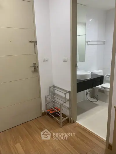 Modern apartment entrance with adjacent bathroom featuring sleek fixtures and wooden flooring.