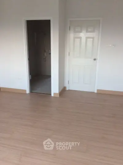 Spacious room with wooden flooring and two doors, ideal for versatile use.