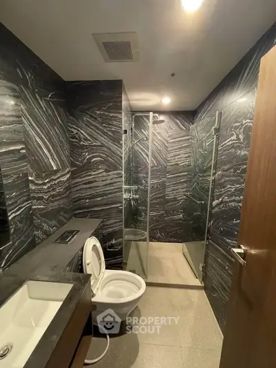 Luxurious modern bathroom with sleek marble walls and glass shower enclosure.