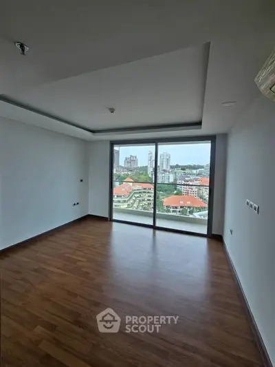 Spacious room with large window offering stunning city view and wooden flooring.