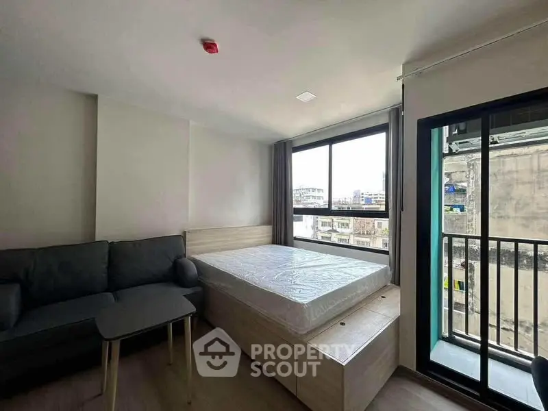 Modern bedroom with large window and city view, featuring a cozy sofa and sleek design.