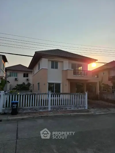 Charming two-story house with balcony and fenced yard in suburban neighborhood at sunset.
