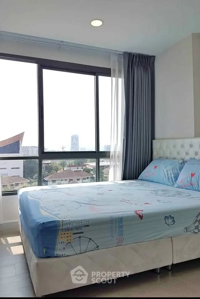 Bright and cozy bedroom with large window offering city views, perfect for relaxation and comfort.