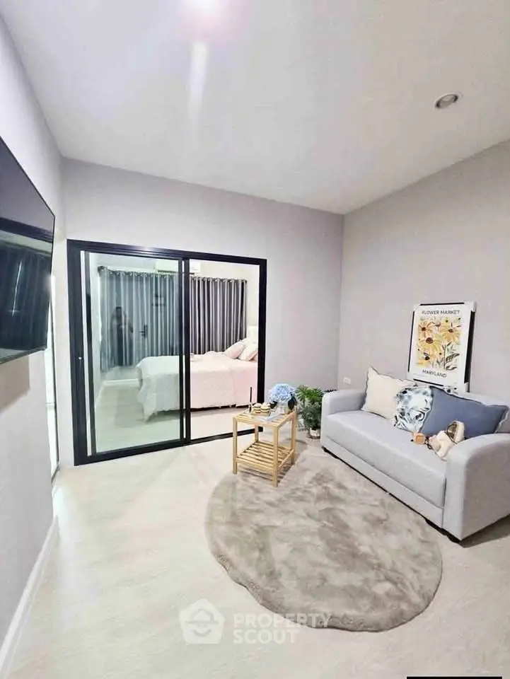 Modern living room with cozy sofa and stylish decor, featuring a view into a chic bedroom through sliding glass doors.