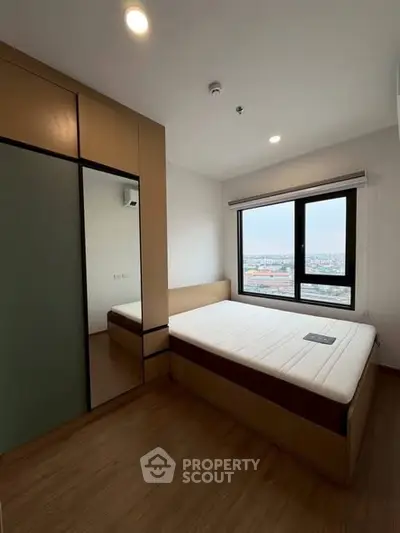 Modern bedroom with large window offering city view, featuring sleek wardrobe and cozy bed.