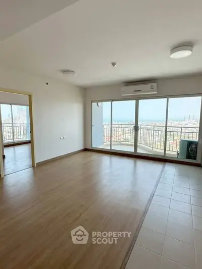 Spacious living room with large windows and city view, featuring wooden flooring and air conditioning.