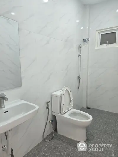 Modern bathroom with sleek white tiles, featuring a toilet, sink, and shower area, offering a clean and minimalist design.