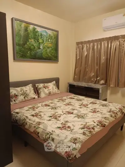 Cozy bedroom with floral bedding and wall art, featuring air conditioning and natural light.