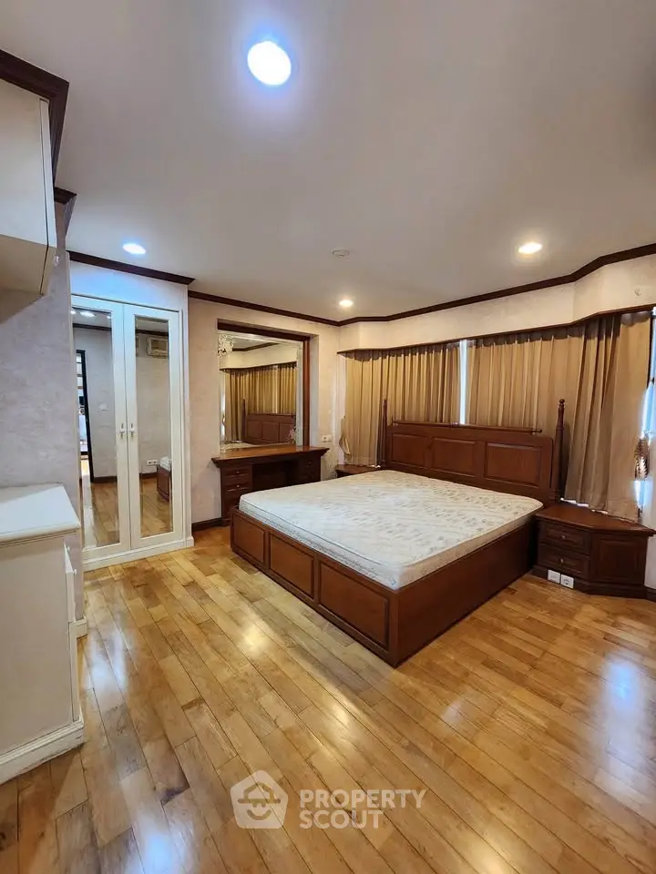 Spacious bedroom with wooden flooring and elegant furnishings in a modern apartment.