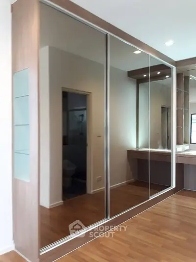 Spacious bedroom with mirrored sliding closet doors and elegant wooden flooring.