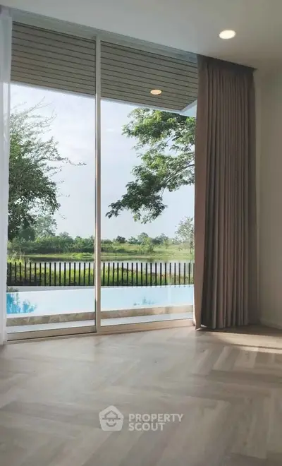 Stunning view from a modern living room with floor-to-ceiling windows overlooking a serene pool and lush greenery.