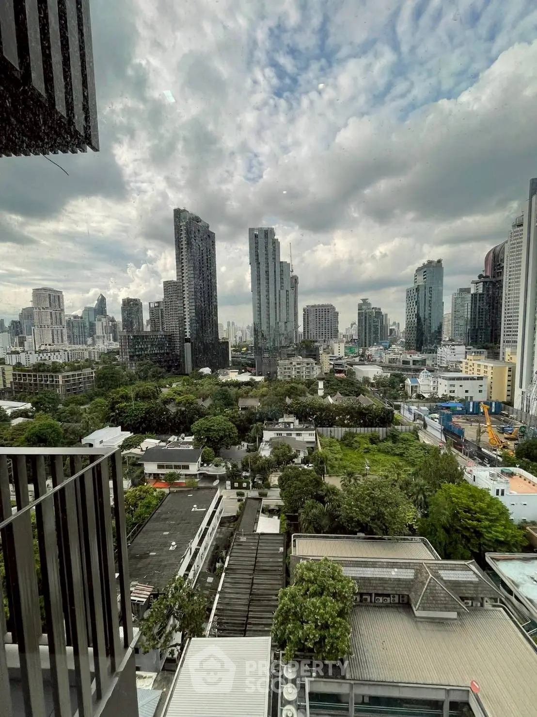 Stunning cityscape view from high-rise balcony overlooking lush greenery and modern skyline.