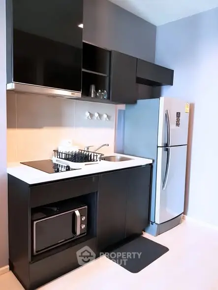 Modern kitchen with sleek black cabinets and stainless steel appliances in a compact layout.