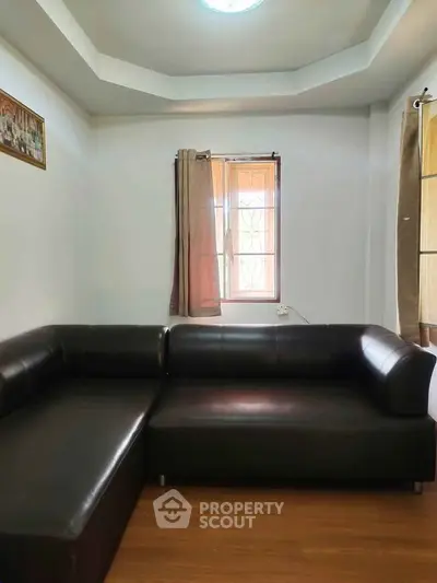 Cozy living room with stylish black leather sectional sofa and natural light from window.